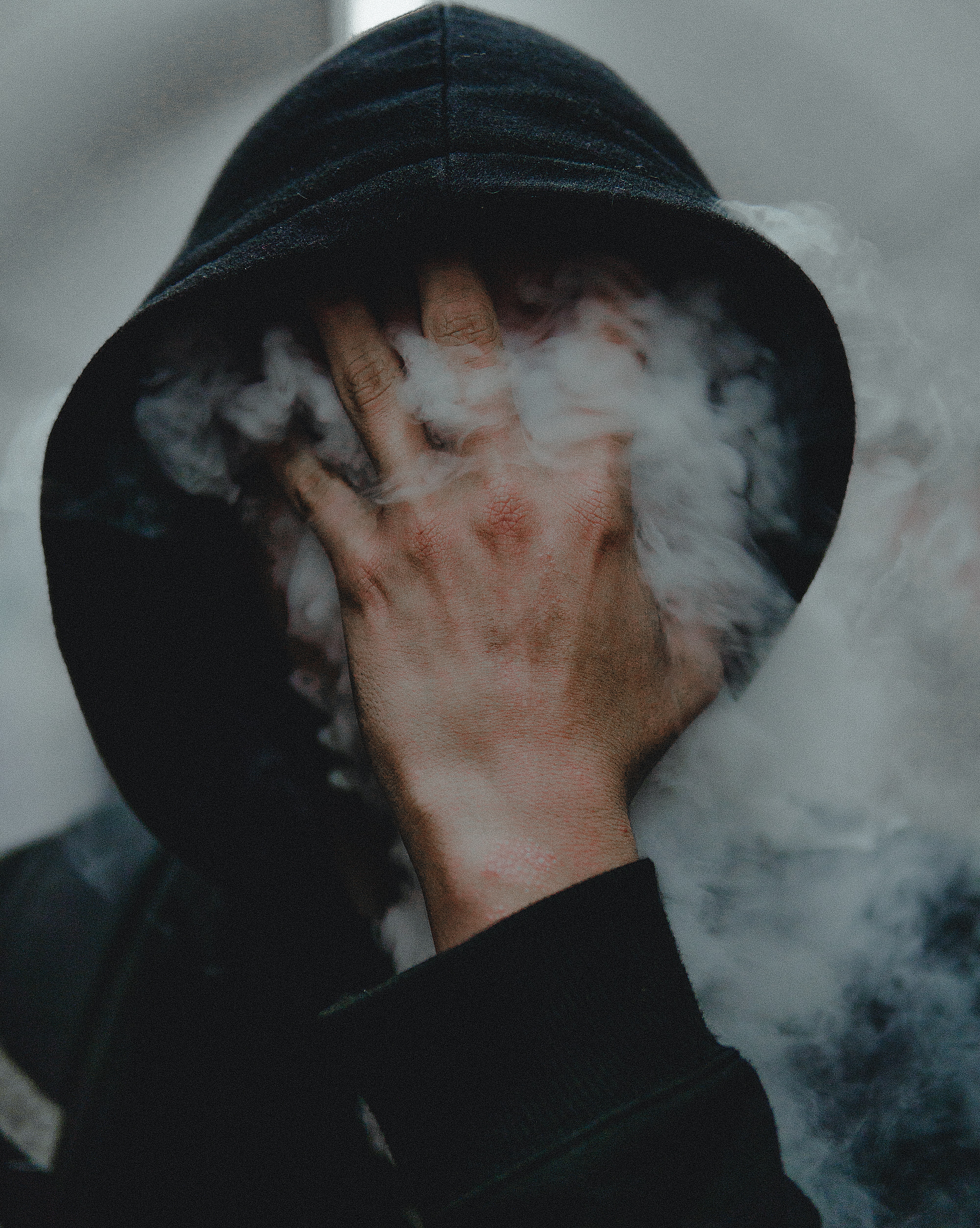 a hooded person hiding their face behind smoke